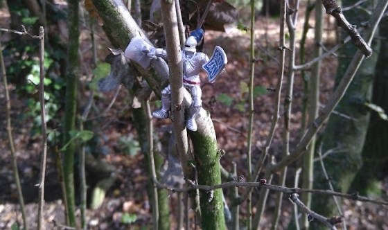 A small toy knight perched on a branch in woodland.