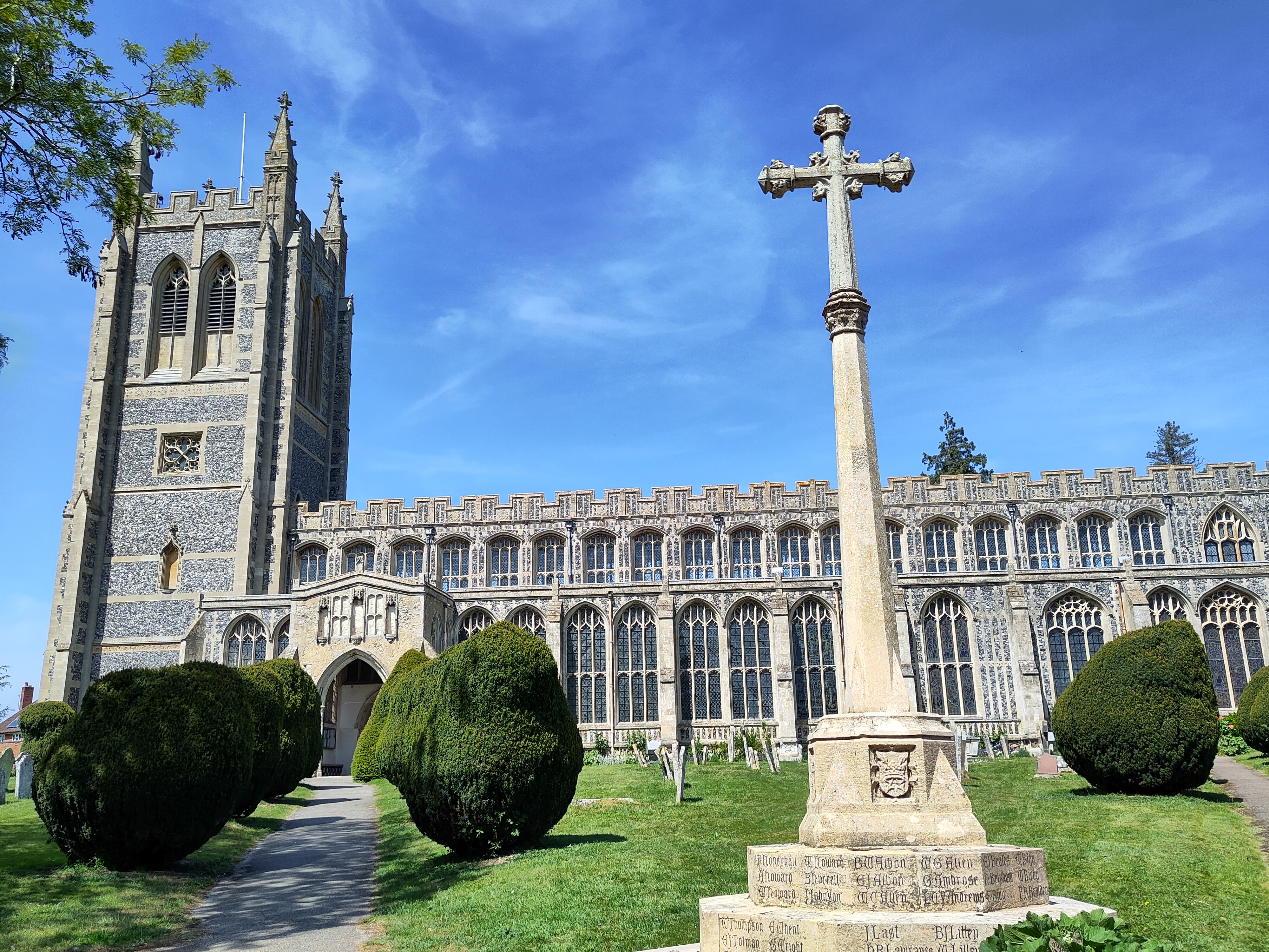 A large Suffolk flint church with stone cross in the foreground.