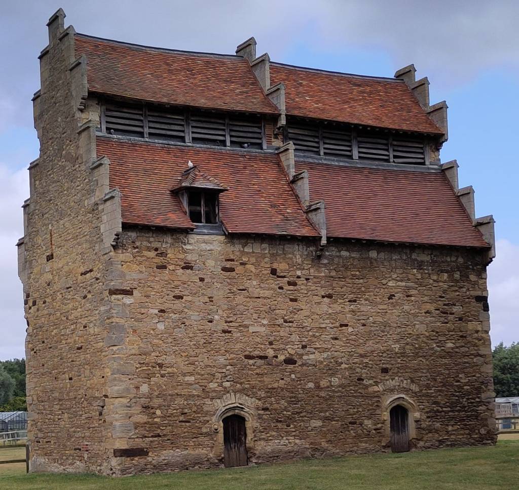 An imposing stone building with steep gables and a tiled roof. There are slats for the birds to enter through.