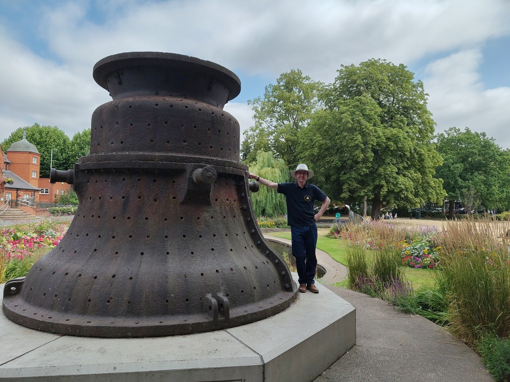 A man in a hat stood next to a large bell case.