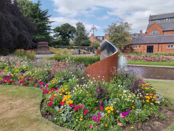 Bell casing in a park. The flowerbeds are full of colourful flowers.