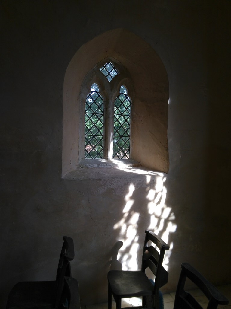 Sunlight through a small plain glass window lights up a wooden chair.