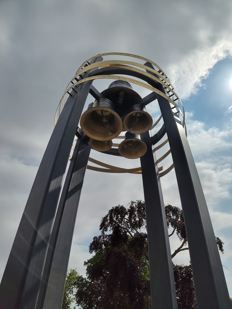 Looking up into four bells surrounded by pillars and golden metal bands.